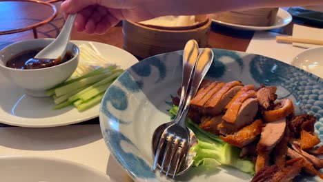 delicious peking duck dish with cucumbers, onions, steamed pancakes and hoisin sauce, picking up hoisin sauce with a spoon, traditional asian food at a restaurant, 4k shot