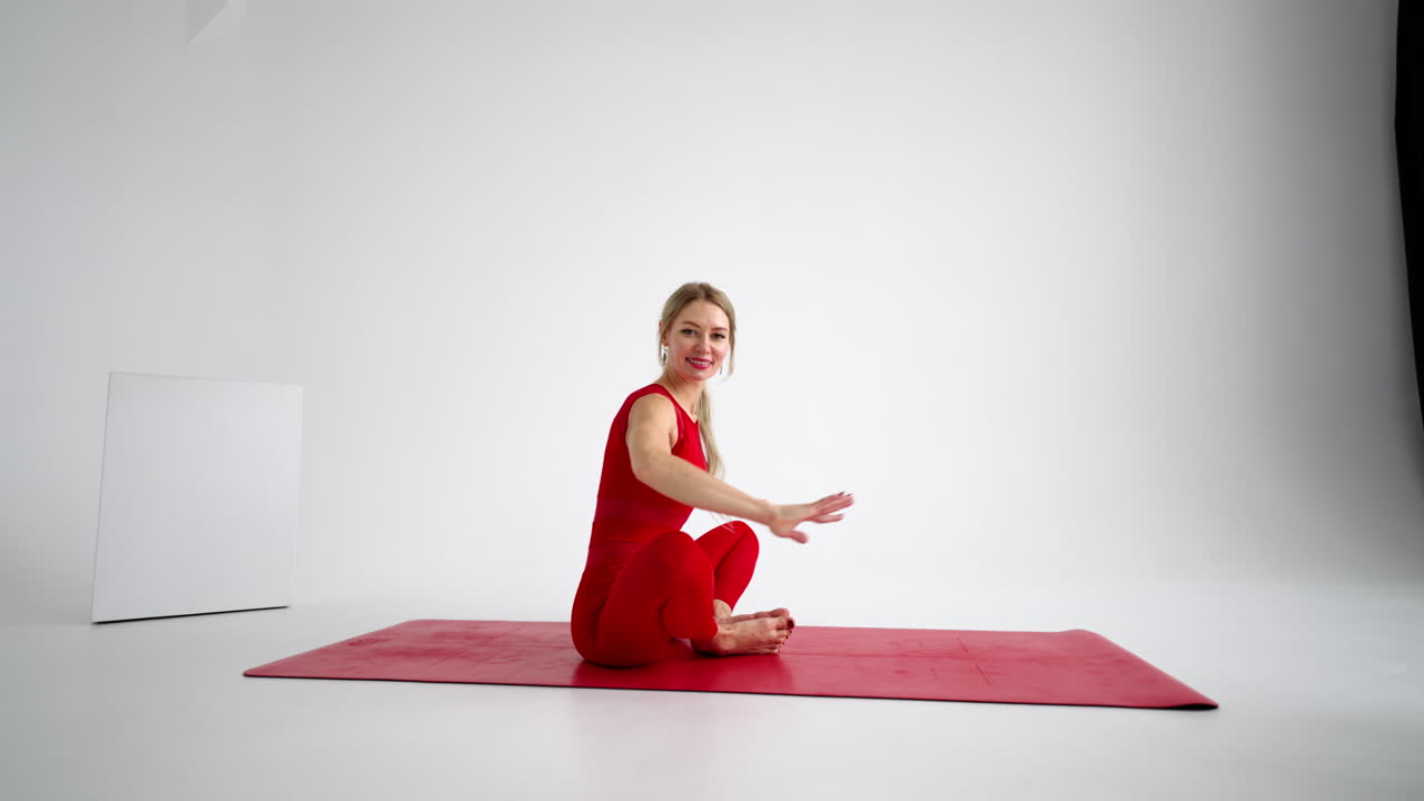 Smuk ung kvinde iført rødt sportstøj laver yoga- eller pilatesøvelse på hvid baggrund.