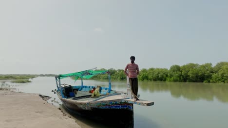 a fisherman balances on the bow of a traditional boat navigating the serene waters of the indus river delta, surrounded by lush mangrove vegetation.