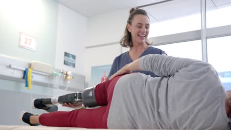 Caucasian-female-physiotherapist-stretching-prosthetic-leg-of-female-patient-at-rehab-center