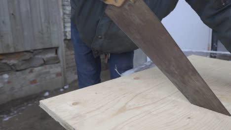 Un-Hombre-Vestido-Con-Una-Chaqueta-Negra-Y-Guantes-Aserrando-Un-Gran-Tablón-De-Madera