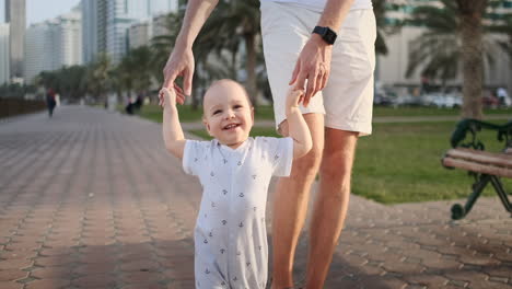 Young-father-with-a-child-and-first-steps.-Young-father-with-a-child-at-outdoor-learninig-for-a-first-steps-near-urban-house-in-the-city