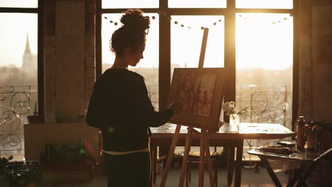 Fully-concentrated-sophisticated-female-artist-in-her-20's-is-drawing-picture-on-easel-in-an-art-studio.