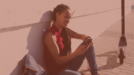 mujer biracial usando un teléfono inteligente sentada al lado de la calle