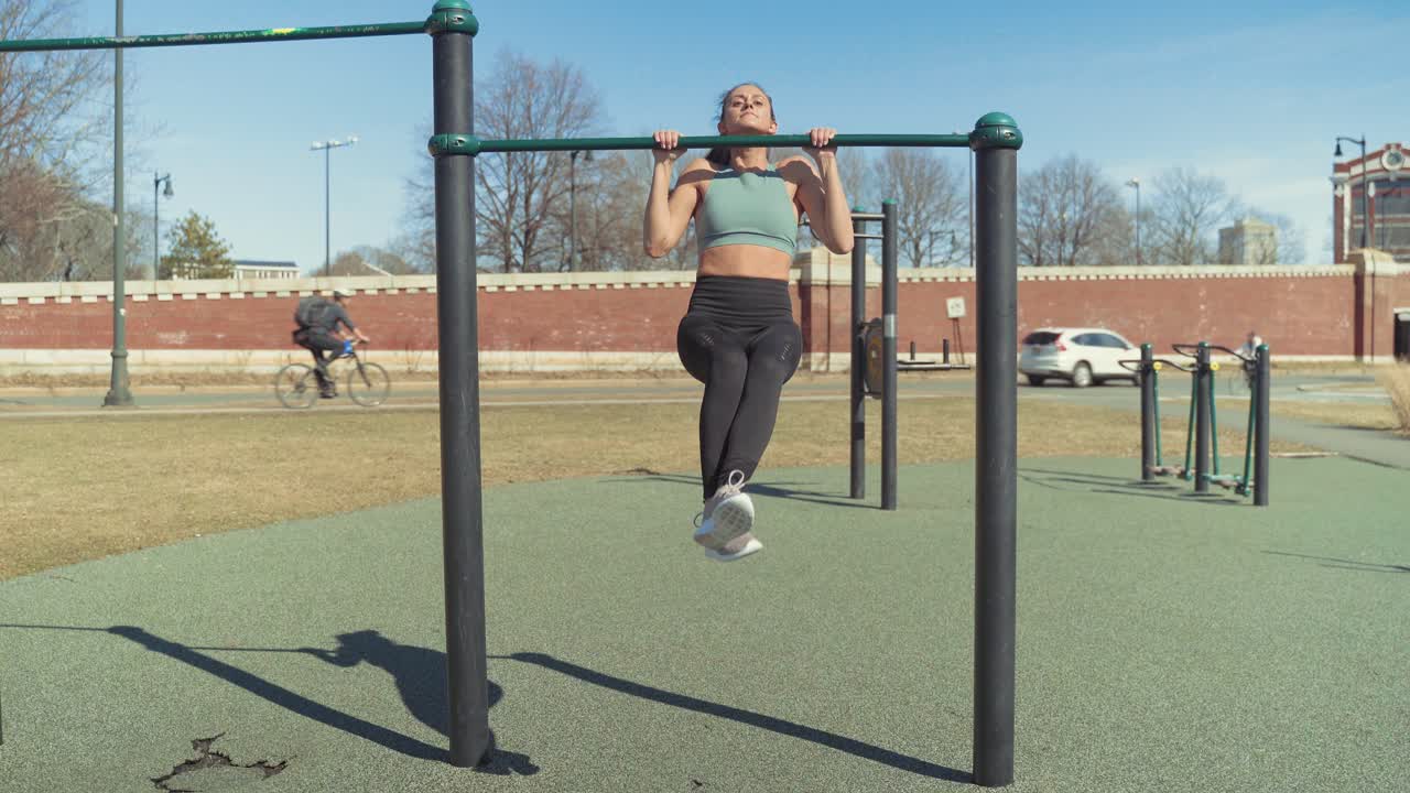 una chica caucásica en forma haciendo ejercicio con ejercicios de dominadas, entrenamiento de fuerza en el gimnasio al aire libre en un día soleado de verano - toma amplia