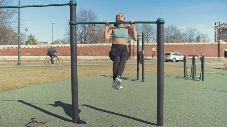 Fit Caucasian Girl Working Out With Pull Up Exercises, Strength Training At Outdoor Gym On Sunny Summer Day - Wide Shot