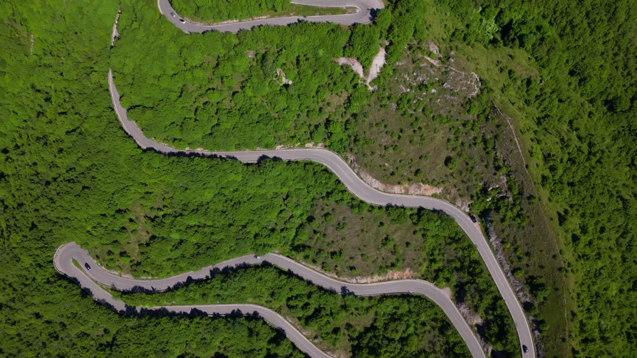Drone top-down of a winding road making sharp turns through lush hillside forest in Selvino. Shot at Selvino, Italy (Selvino, Italia)