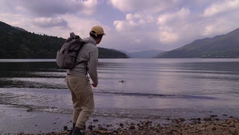 male hiker skipping stone on beautiful lake in pristine nature setting