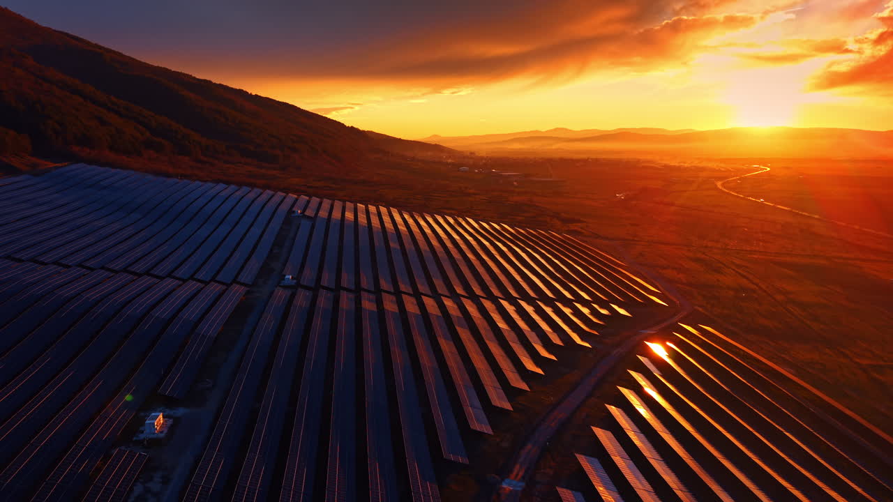 Rækker af solpaneler under intens gylden solnedgang. Luftfoto af fotovoltaiske paneler vendt mod den nedgående sol med gyldent lys og lange skygger i et landligt bjergområde.