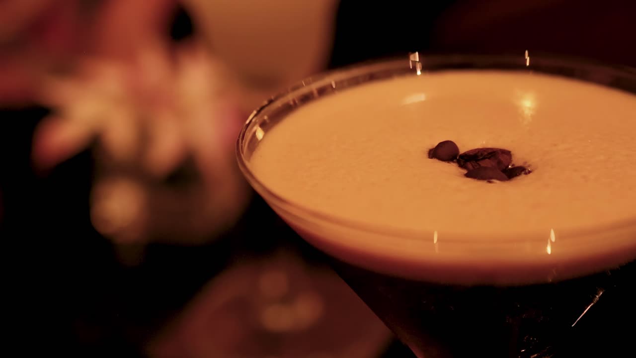Uma vista detalhada de um espresso martini guarnecido com grãos de café em um ambiente com pouca luz