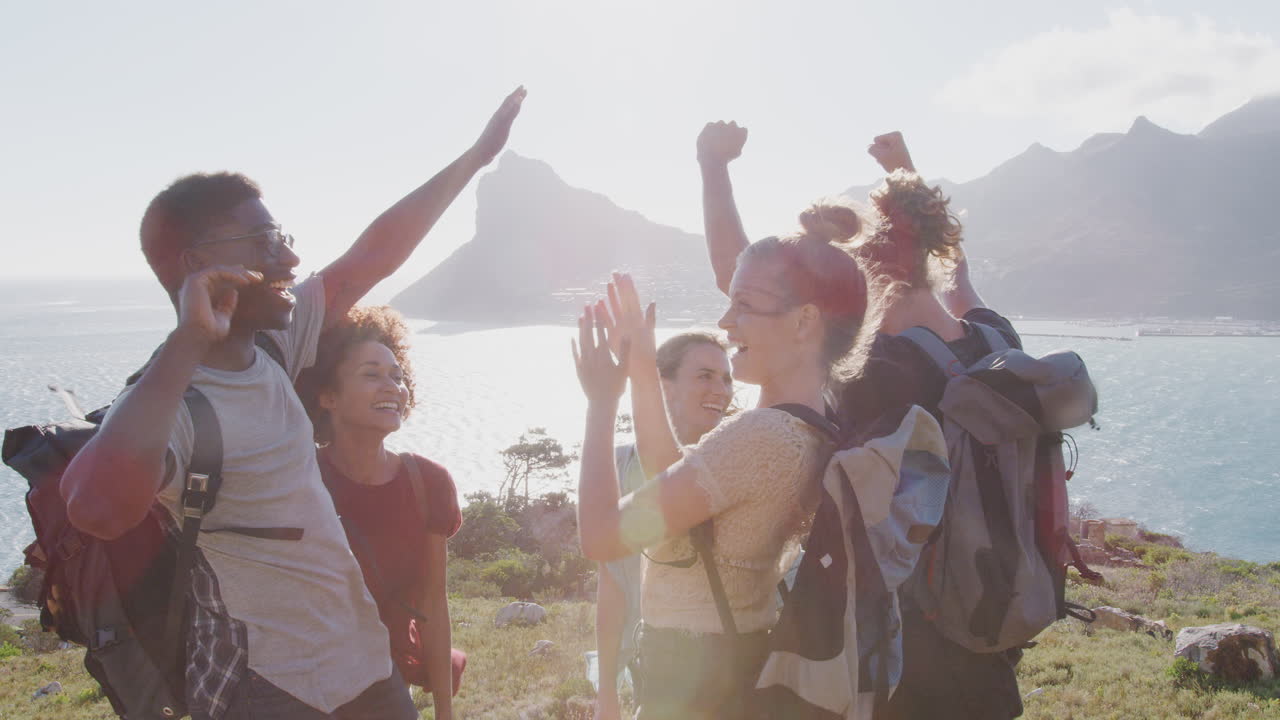 grupo de jóvenes amigos de senderismo celebrando llegar a la cima del acantilado costero