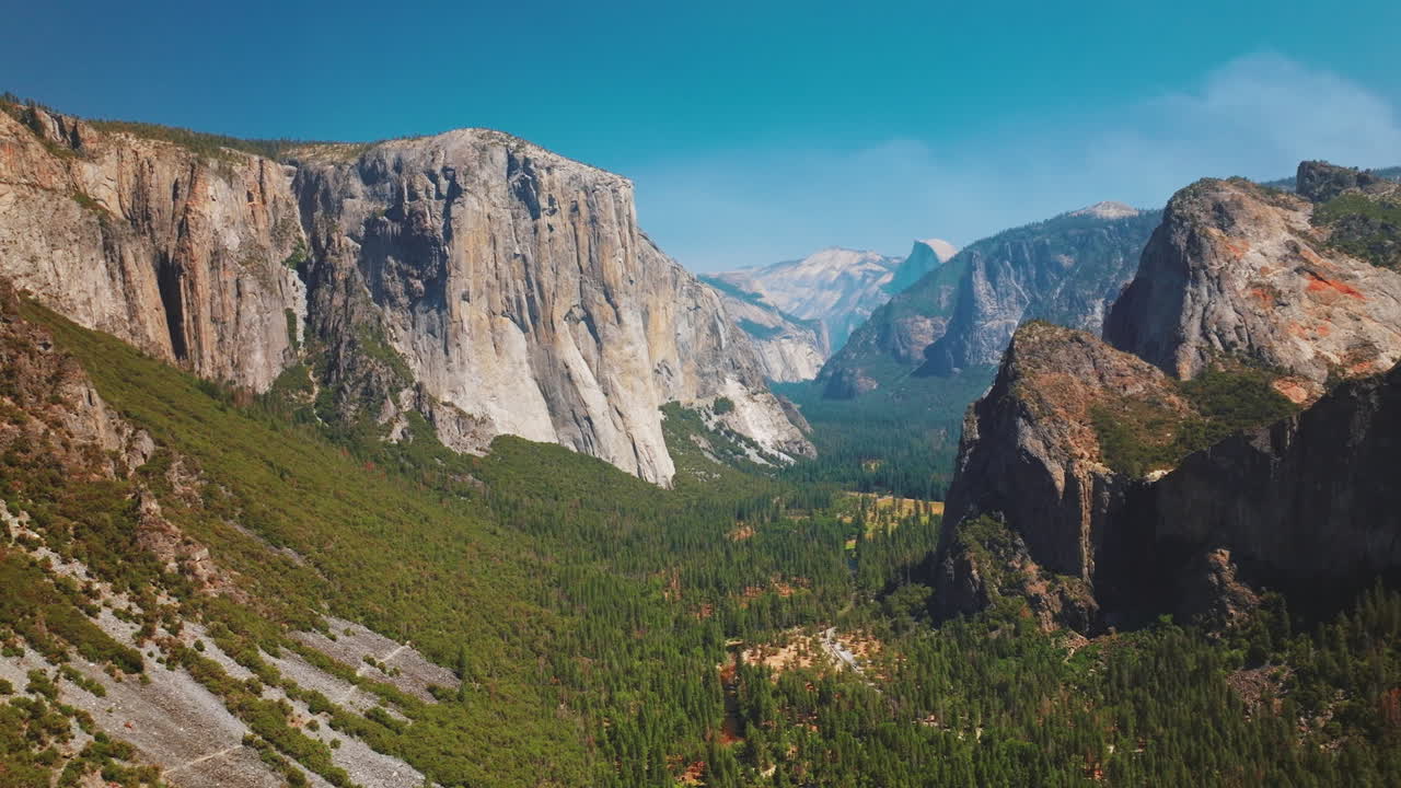 Enormous steep rocks in Yosemite National Park, California, USA. Green pine tree forests growing between the cliffs. Sunny day footage.
