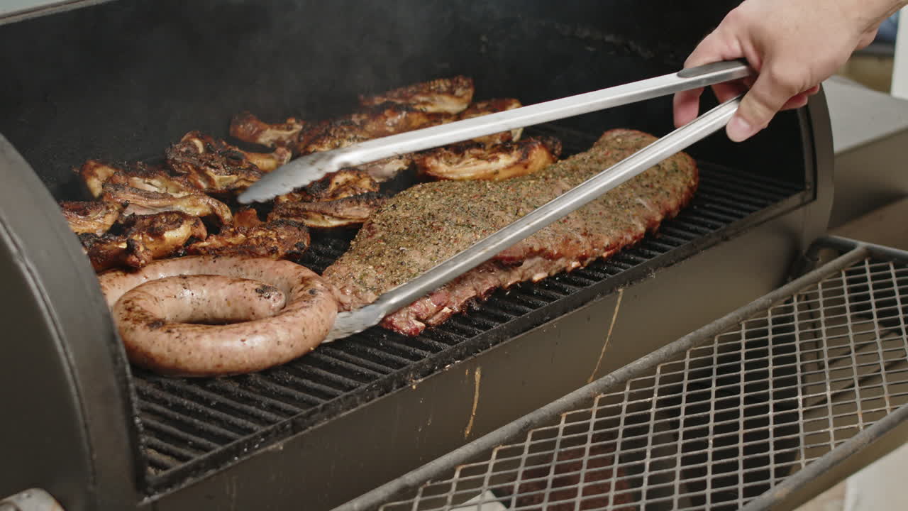 BBQ sausage being flipped on a smoking grill with tongs