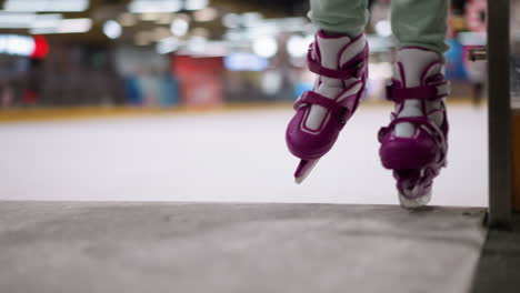 close-up view of a person wearing purple ice skates stepping onto the ice rink, with a blurred view of people skating in the background