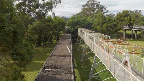 Toma-Aérea-En-Movimiento-Hacia-Adelante-De-Un-Niño-Pequeño-Corriendo-En-Un-Puente-De-Metal-Al-Lado-De-Un-Viejo-Puente-Ferroviario-De-Madera