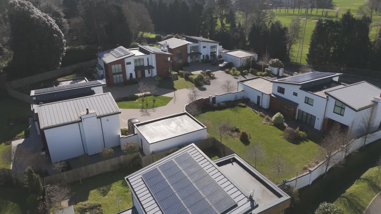 Close aerial of angular grey-and-white houses with integrated garages and large solar arrays reflecting high-efficiency upscale living