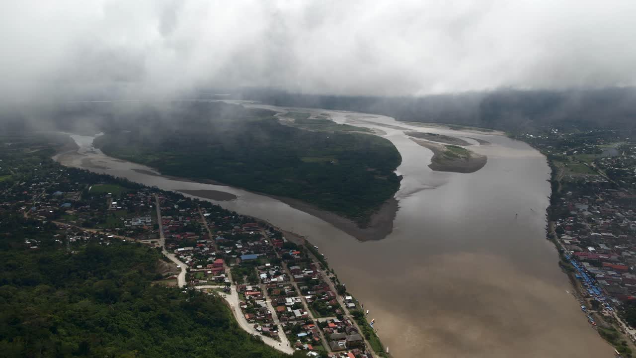 River meanders through the dense jungle near Rurrenabaque, Bolivia, stunning aerial establishing into clouds above homes built on riverbanks
