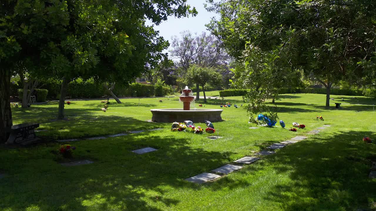 una toma aérea baja de un dolly volando sobre tumbas floridas hacia una fuente decorativa en una morgue en california