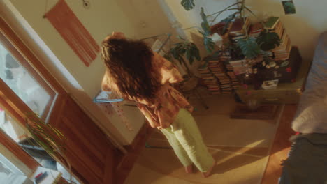 young woman, deep in thought, walking through cozy sunlit bedroom