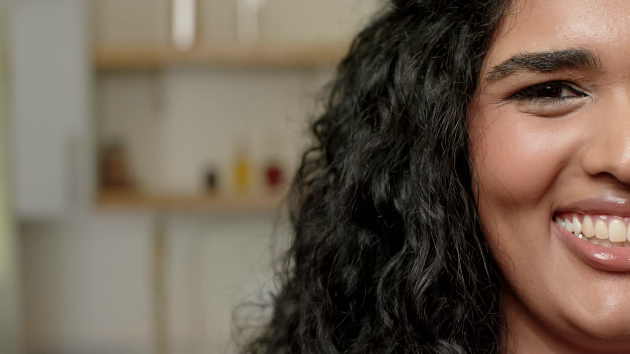 Femme indienne adulte souriant, clignant des yeux tandis que la caméra réalise un gros plan à droite, chez elle avec des bocaux, espace pour texte.