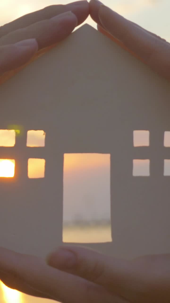 Hands Protecting a Paper House at Sunset