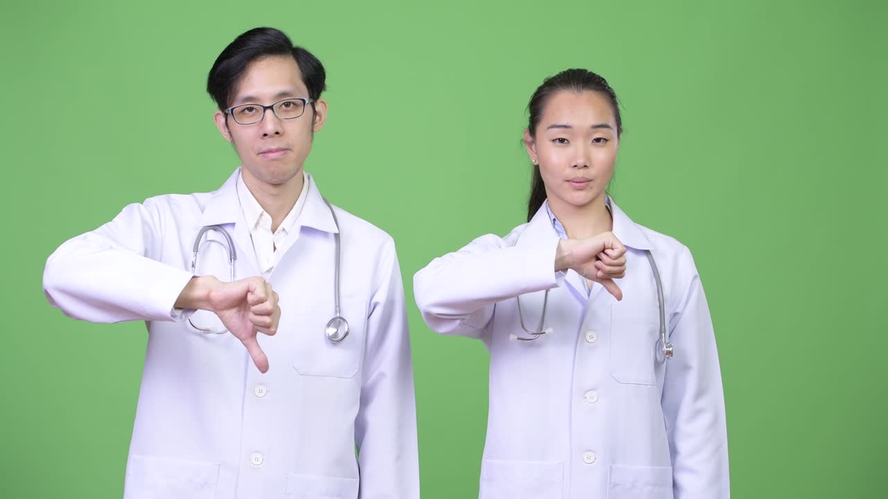 Young Asian couple doctors giving thumbs down together