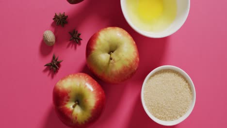 Video-of-baking-ingredients,-rolling-pin-and-apples-lying-on-pink-background