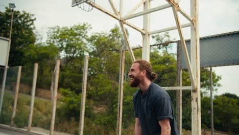 A-red-haired-man-in-a-gray-t-shirt-scores-a-goal-in-a-basketball-hoop-and-rejoices-in-his-success-on-the-basketball-court