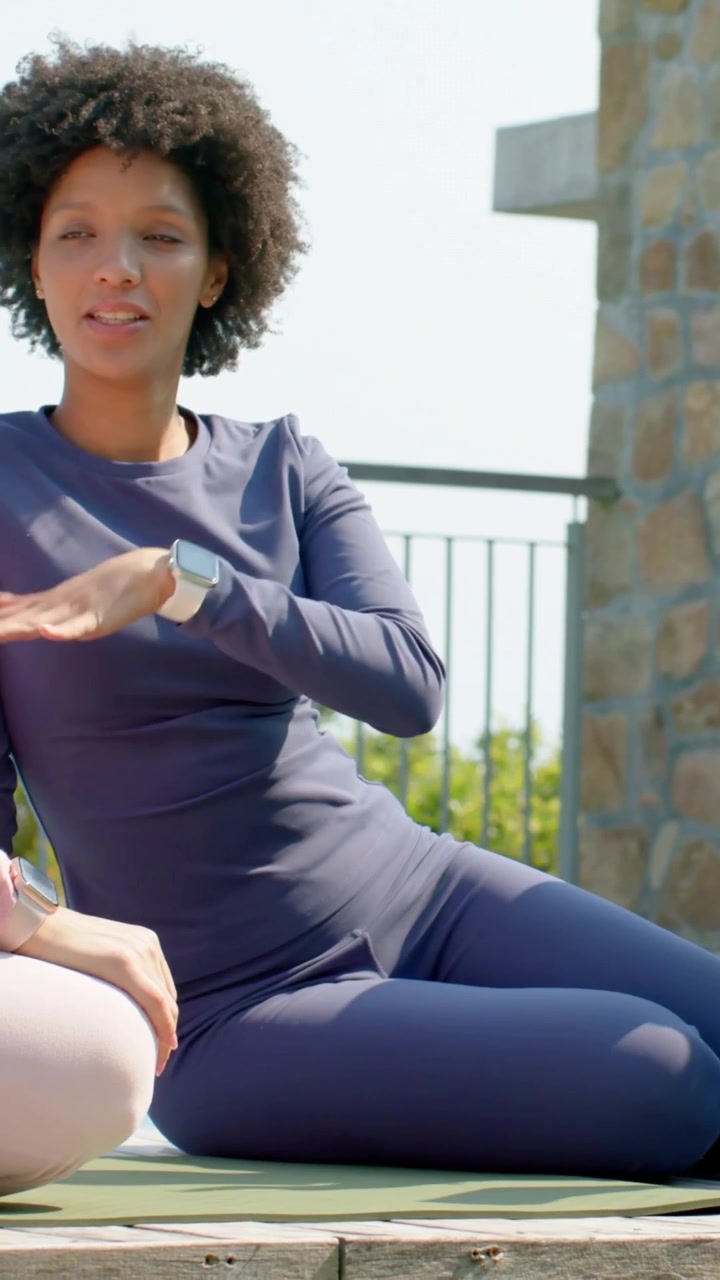 Video verticale: Donna sorridente in leggings che risponde a un'amica e tocca l'orologio su un tappetino da yoga sul tetto