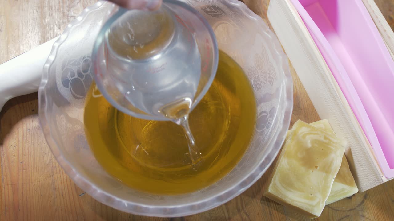 Versare la soluzione di liscivia negli oli per la produzione di sapone a freddo.