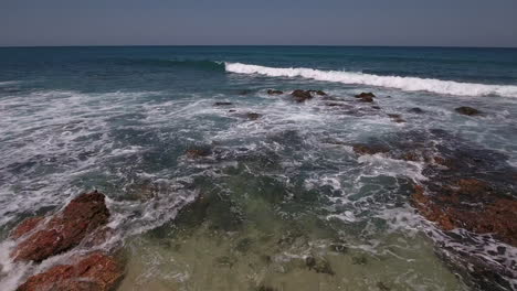 Drone-De-Bajo-Vuelo-Sobre-Olas-Que-Vuelan-Hacia-El-Océano-En-Una-Playa-Rocosa-En-Cabo-San-Lucas,-México