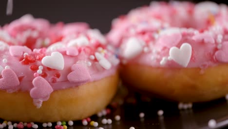 sprinkles falling onto pink donuts with heart shaped sprinkles - sliding shot