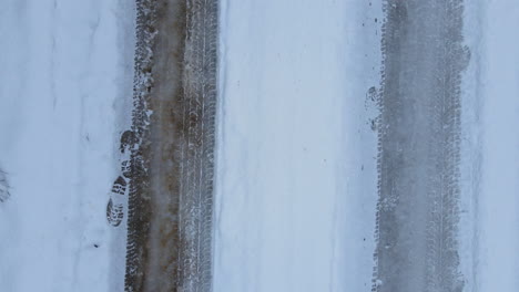 Top-down-tyre-tracks-on-snow-on-a-snow-covered-road,-slow-motion-regular-back-track