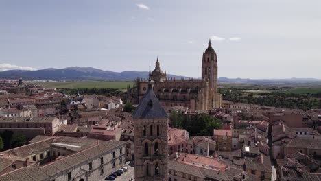 Establishing-aerial-view-across-the-rooftops-of-San-Estaban-church-and-Segovia-cathedral-with-mountain-landscape-skyline