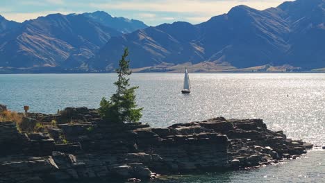 Un-Recorrido-Aéreo-En-Camión-Alrededor-De-Una-Isla-Rocosa-Revela-Un-Velero-Flotando-Tranquilamente-En-Medio-Del-Lago