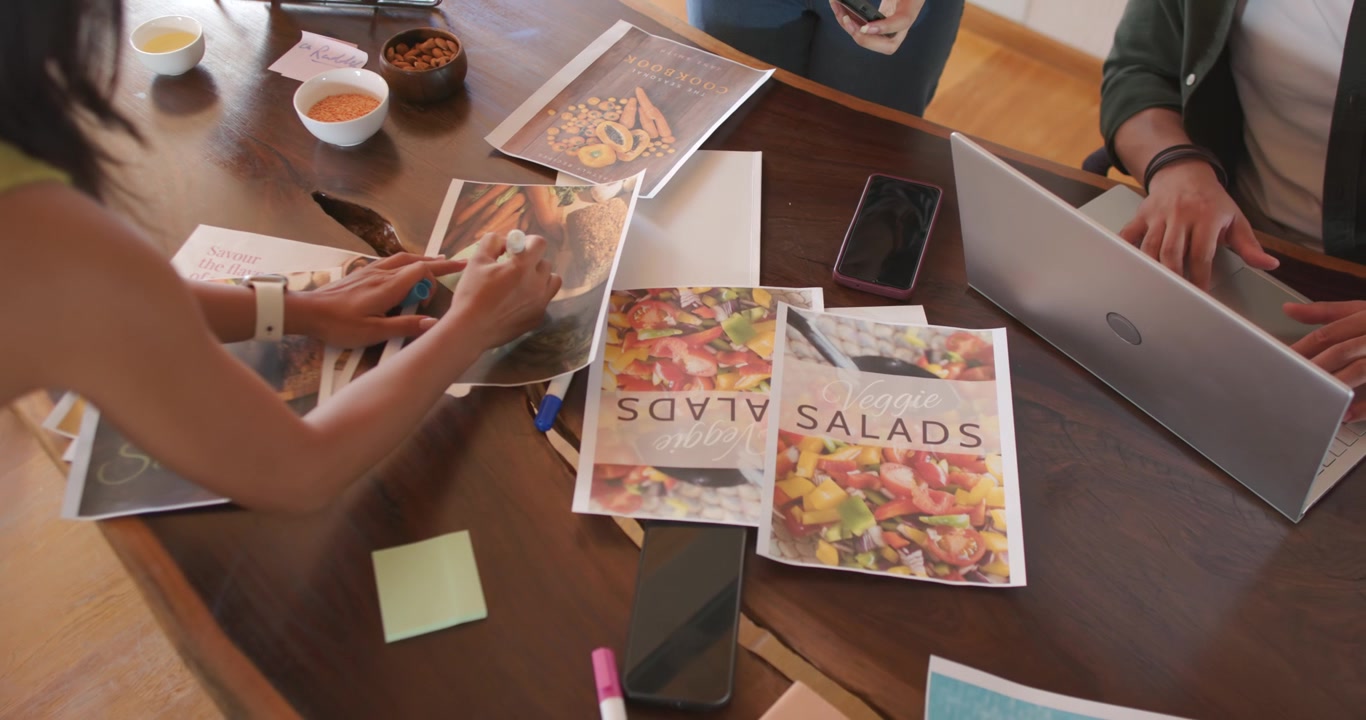 Forskellige kolleger præsenterer nye print og kommenterer SALADS-brochurer ved et træbord med henblik på redesign.