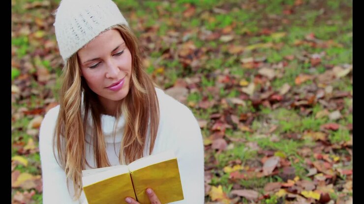 Donna che legge un libro al parco in una giornata autunnale.