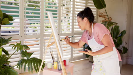 woman painting on canvas using paintbrush and palette in home studio