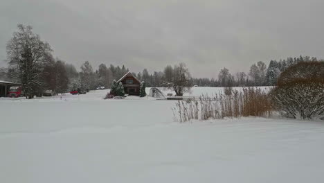 pan shot from right to left of wooden cottages surrounded by snow all around from snowfall on a cloudy day