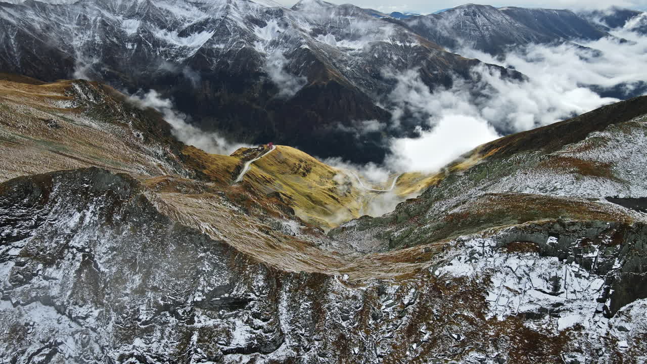 Aerial drone view of nature in Romania. Transfagarasan route in Carpathian mountains, snow on mountains rocky slopes, valley, clouds