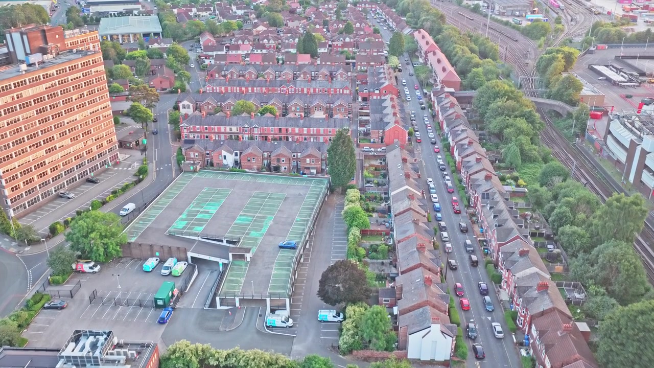 Victoriaanse rijtjeshuizenbuurt nabij Old Trafford, Manchester, Engeland, Verenigd Koninkrijk, met bakstenen huizen, woonstraten, tennisbanen en spoorwegcorridor, drone-overvlucht voorwaarts