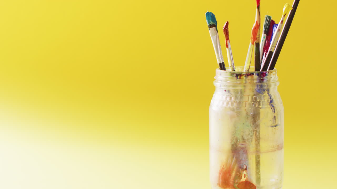 video de una colección de pinceles usados de pie en un frasco sobre un fondo amarillo con espacio de copia