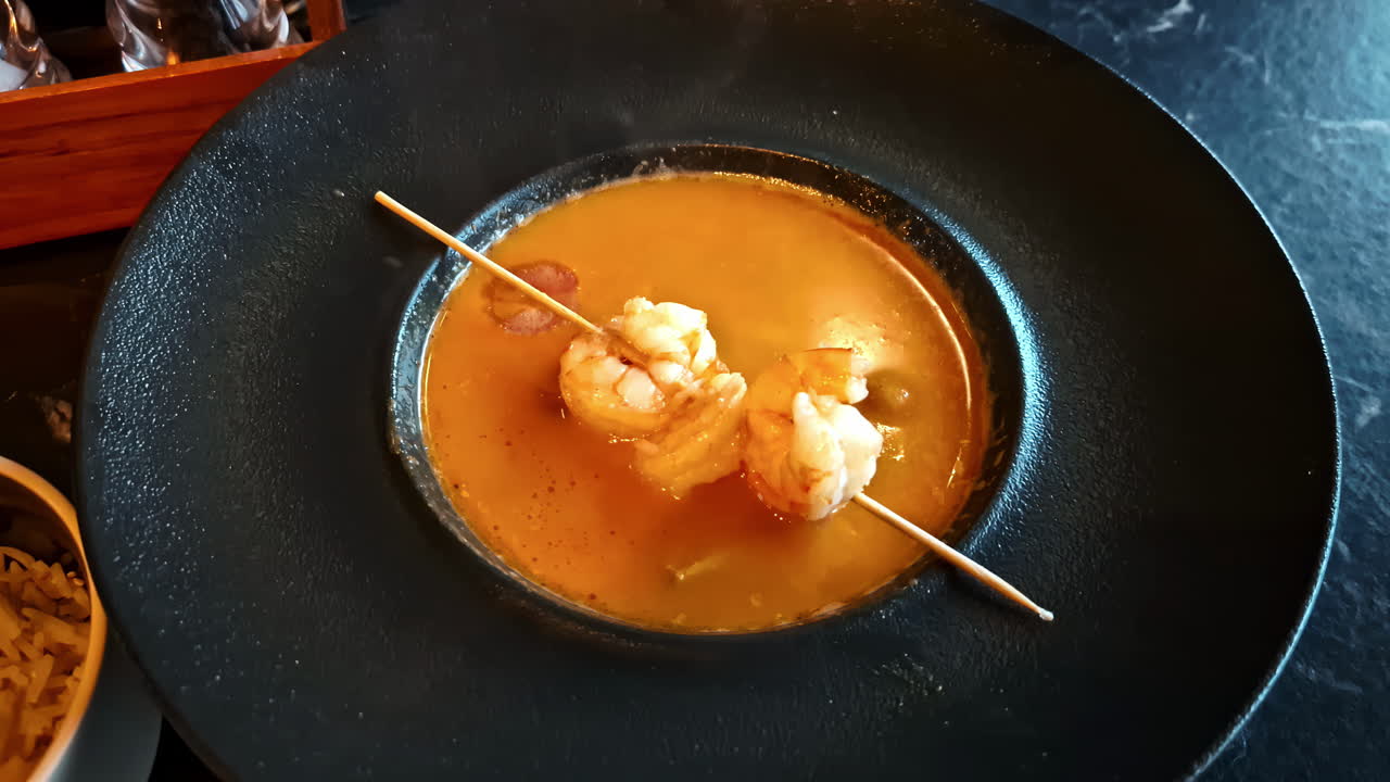 Slow horizontal zoom reveals perfectly peeled shrimp glistening in rich, vibrant orange sauce inside a dark bowl — an irresistible gourmet seafood moment