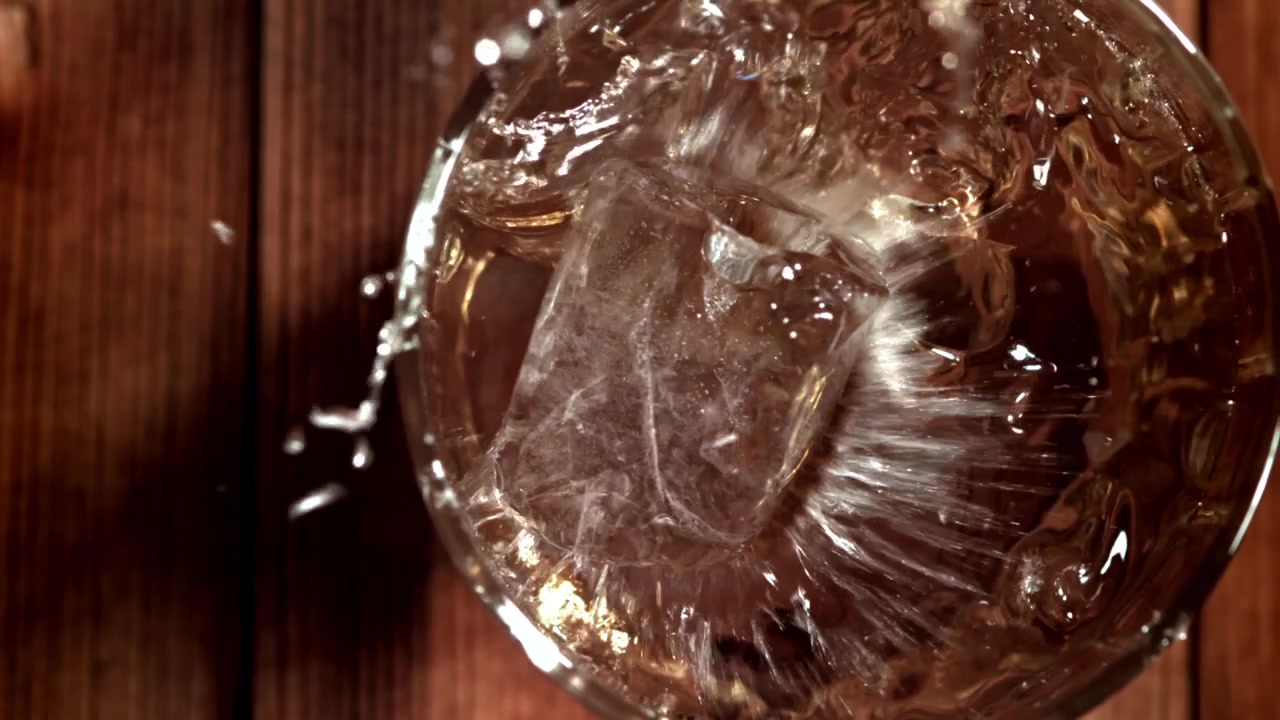 Liquido Dorato Versato in un Bicchiere con Cubetto di Ghiaccio al Rallentatore