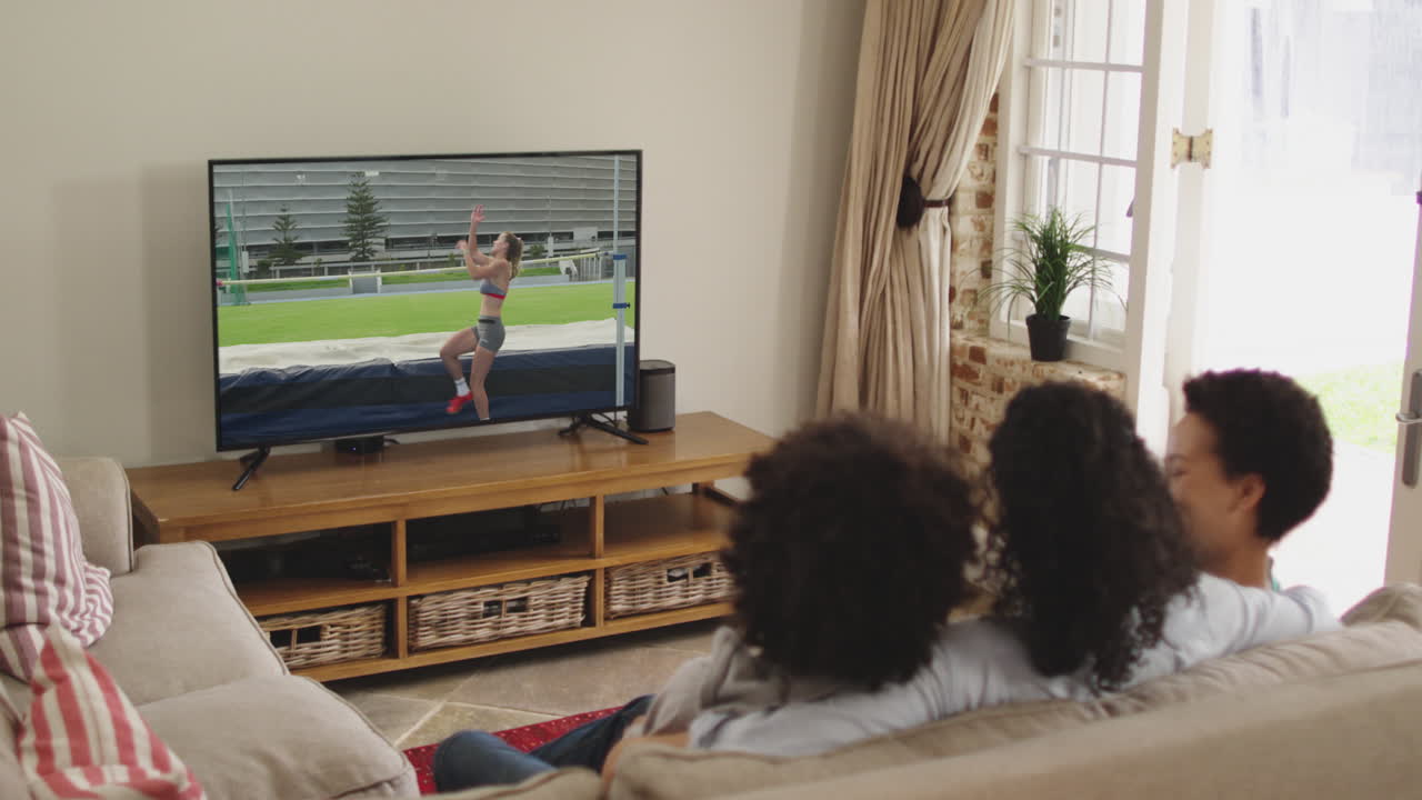 Famiglia felice seduta a casa insieme che guarda l'atletica salto in alto in TV