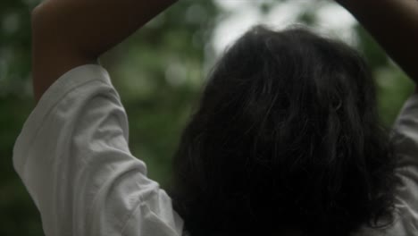 young woman in a white t-shirt is stretching her arms with a blurred forest background in close-up view