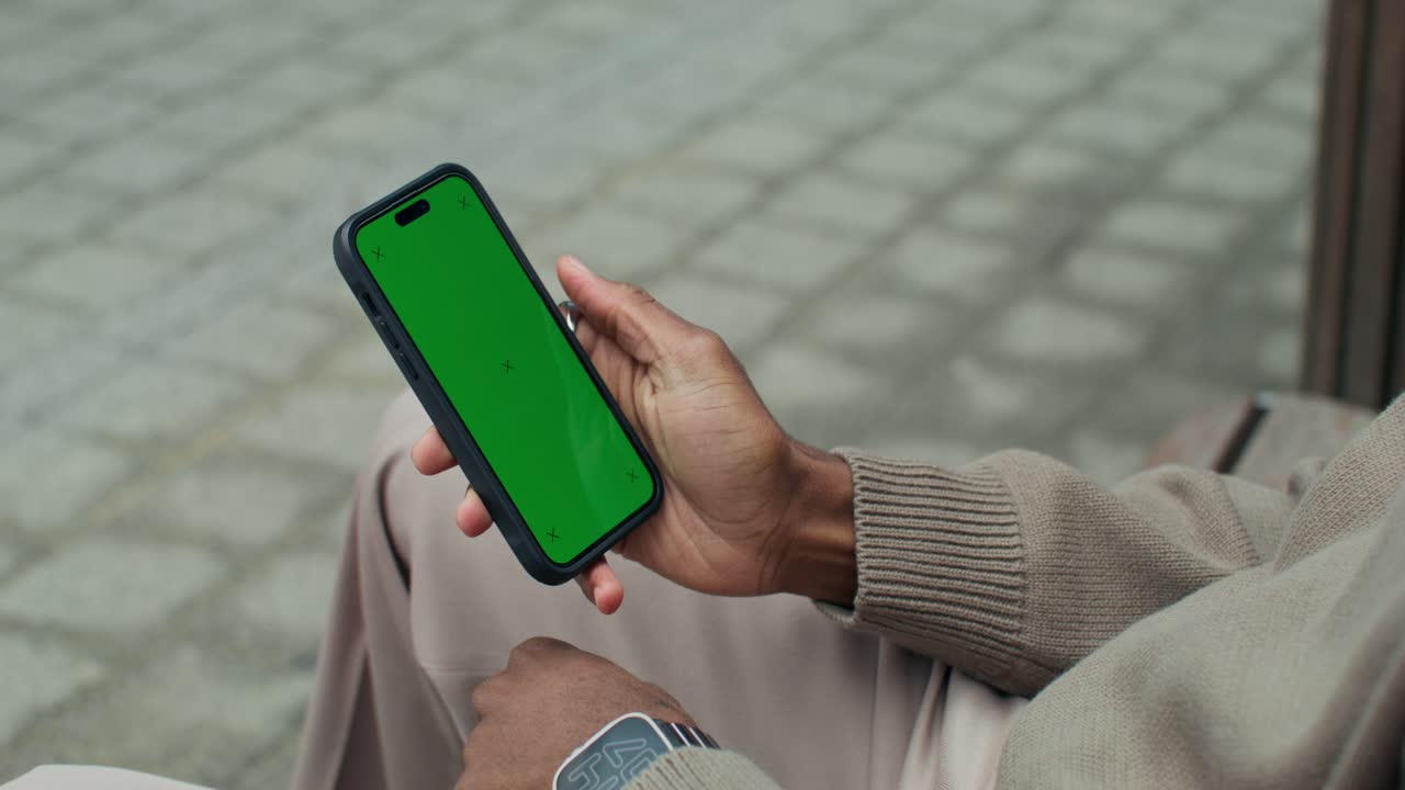 Person, der holder en smartphone med en grøn skærm udendørs