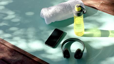 Towel, bottle of water, headphones and smartphone on yoga mat at log cabin, slow motion