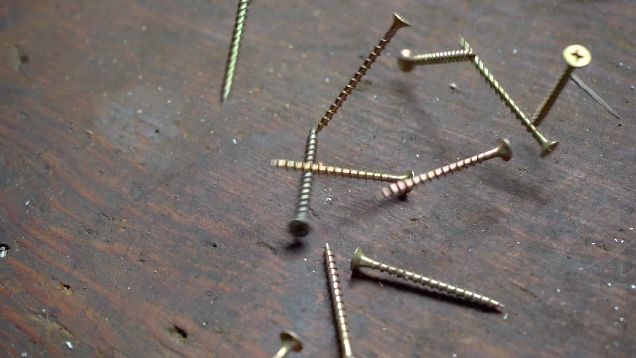 imágenes en cámara lenta de un montón de tornillos cayendo sobre un banco de trabajo de madera
