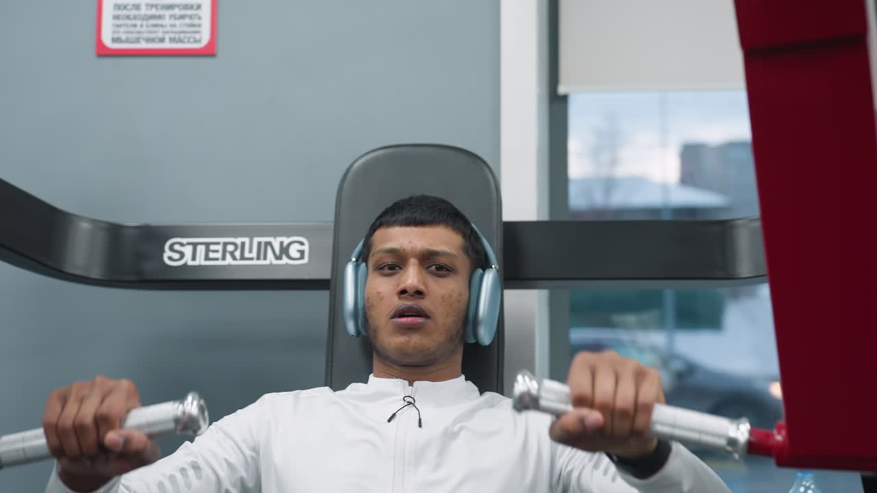 fitness coach gripping handles of chest press machine during strength training in modern gym while focused on building upper body muscles with exercise equipment